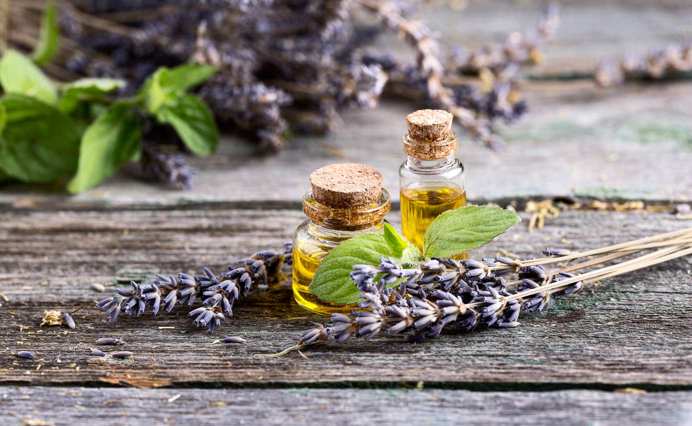 Ätherische Öle und Lavendelblüten auf einem Holztisch, symbolisch für die heilende Wirkung der Aromatherapie. Die Aromatherapie verwendet ätherische Öle, um physische und psychische Beschwerden zu lindern.
