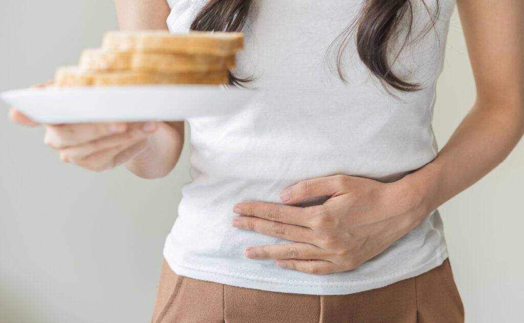Frau hält sich den Bauch und einen Teller mit Toastbrot, ein Hinweis auf vermutete Glutenunverträglichkeit. Eine neue Studie zeigt, dass der Nocebo-Effekt eine Rolle bei nicht-zöliakischer Glutensensitivität spielen könnte.