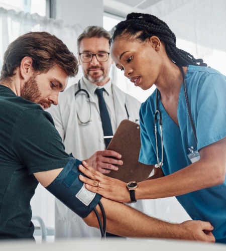 Eine Krankenschwester misst den Blutdruck eines Patienten unter der Aufsicht eines Arztes. Der Artikel beleuchtet integrative Ansätze zur natürlichen Bekämpfung von Bluthochdruck, kombiniert klassische und alternative Therapieansätze zur Optimierung der Gesundheitsprognose.