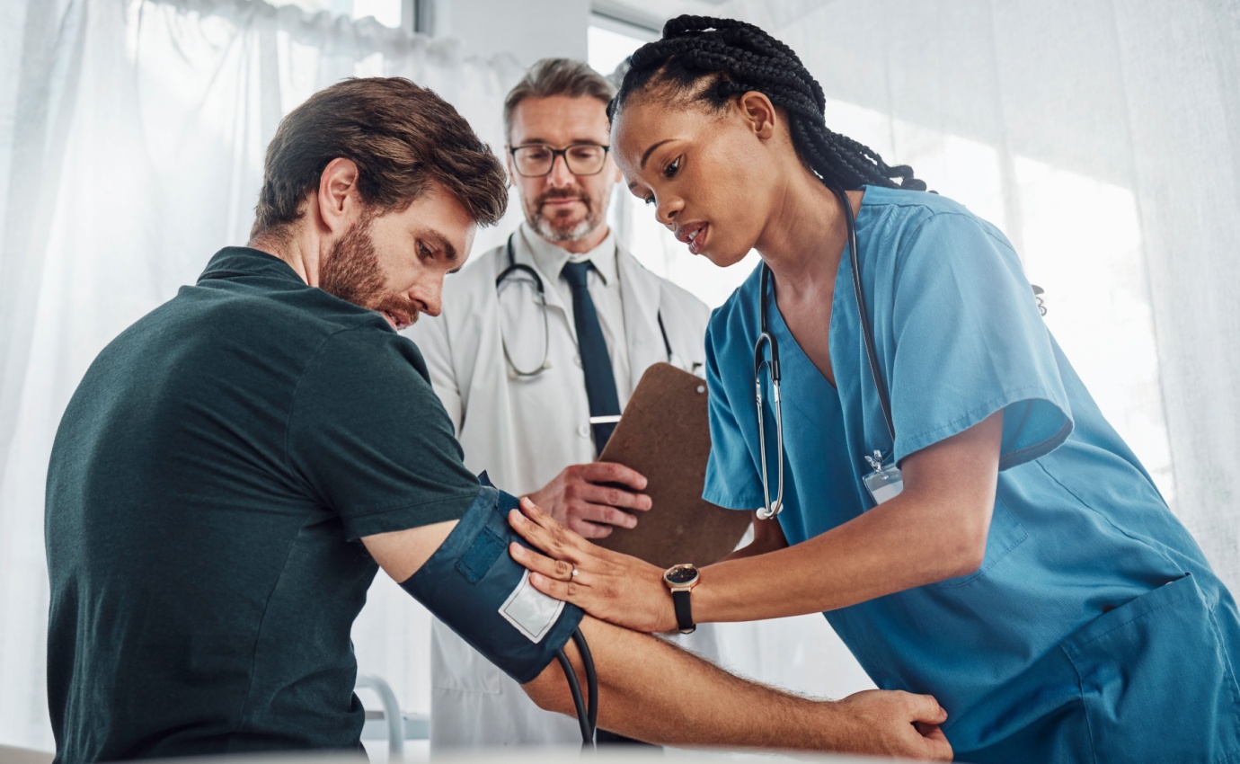 Eine Krankenschwester misst den Blutdruck eines Patienten unter der Aufsicht eines Arztes. Der Artikel beleuchtet integrative Ansätze zur natürlichen Bekämpfung von Bluthochdruck, kombiniert klassische und alternative Therapieansätze zur Optimierung der Gesundheitsprognose.