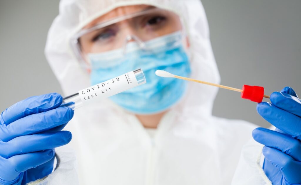 Medizinisches Fachpersonal in Schutzkleidung hält ein COVID-19-Testkit mit einem Abstrichtupfer bereit. Der Artikel untersucht die potenzielle Rolle der Ozontherapie als ergänzende Behandlungsmethode gegen COVID-19.