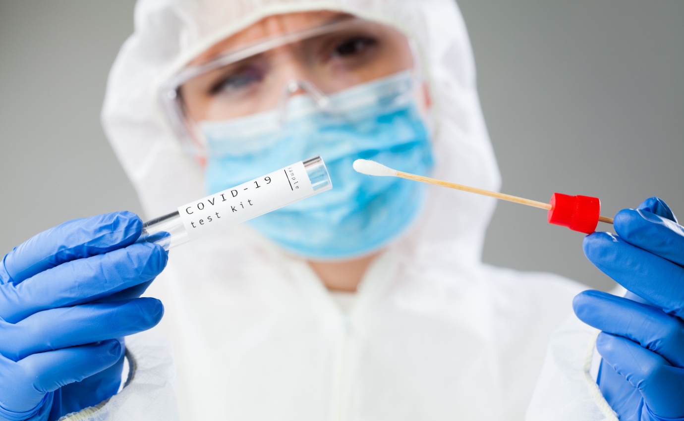 Medizinisches Fachpersonal in Schutzkleidung hält ein COVID-19-Testkit mit einem Abstrichtupfer bereit. Der Artikel untersucht die potenzielle Rolle der Ozontherapie als ergänzende Behandlungsmethode gegen COVID-19.