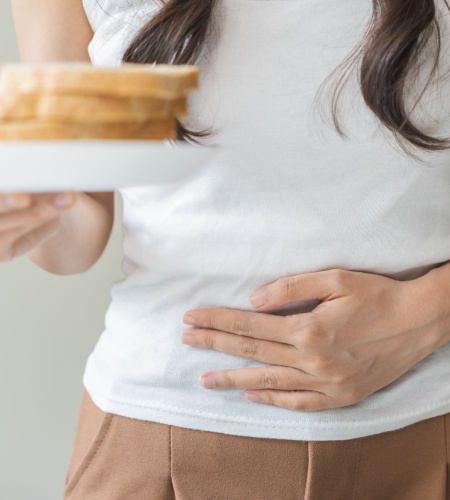 Frau hält sich den Bauch und einen Teller mit Toastbrot, ein Hinweis auf vermutete Glutenunverträglichkeit. Eine neue Studie zeigt, dass der Nocebo-Effekt eine Rolle bei nicht-zöliakischer Glutensensitivität spielen könnte.