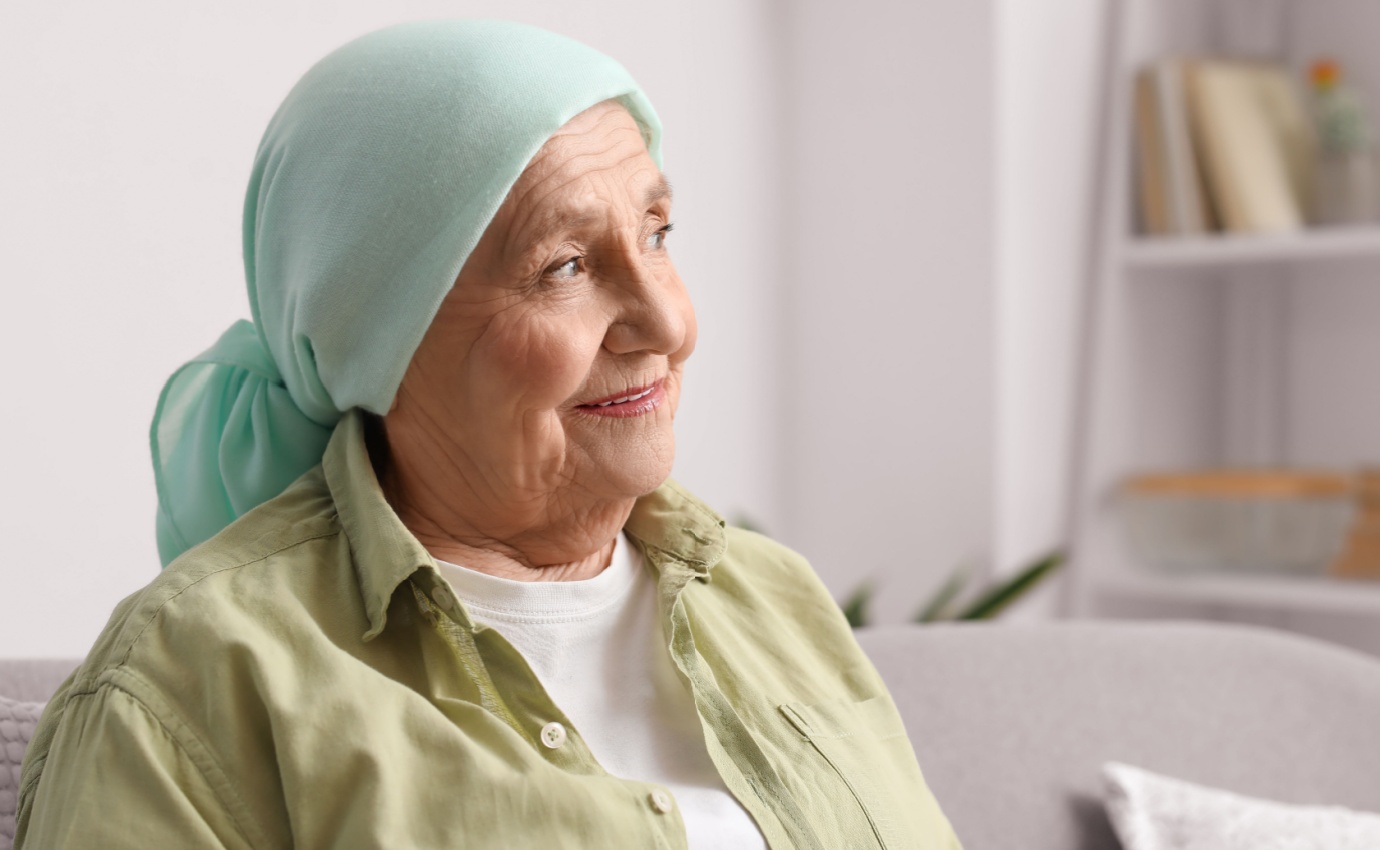 Seniorin mit Kopftuch sitzt nach einer Krebsbehandlung zuversichtlich auf dem Sofa. Dieses Bild veranschaulicht die Rolle komplementärer Therapien bei der Verbesserung der Lebensqualität von Krebspatienten.