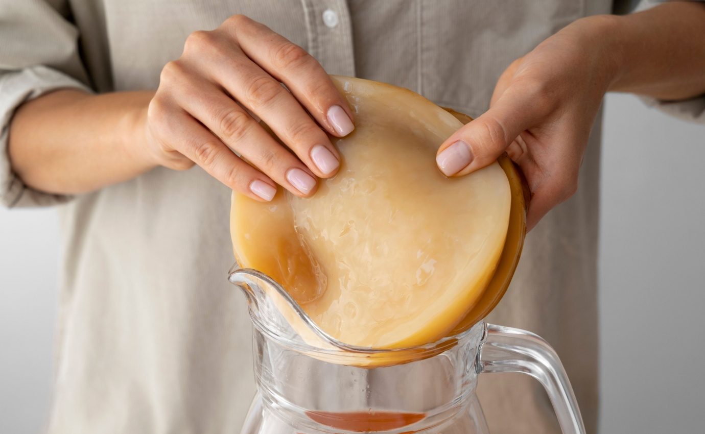 Nahaufnahme einer Person, die eine Kombucha-SCOBY in eine Glaskaraffe legt. Der Artikel untersucht die gesundheitlichen Vorteile von Kombucha bei Stoffwechselerkrankungen und beleuchtet aktuelle Forschungsergebnisse.
