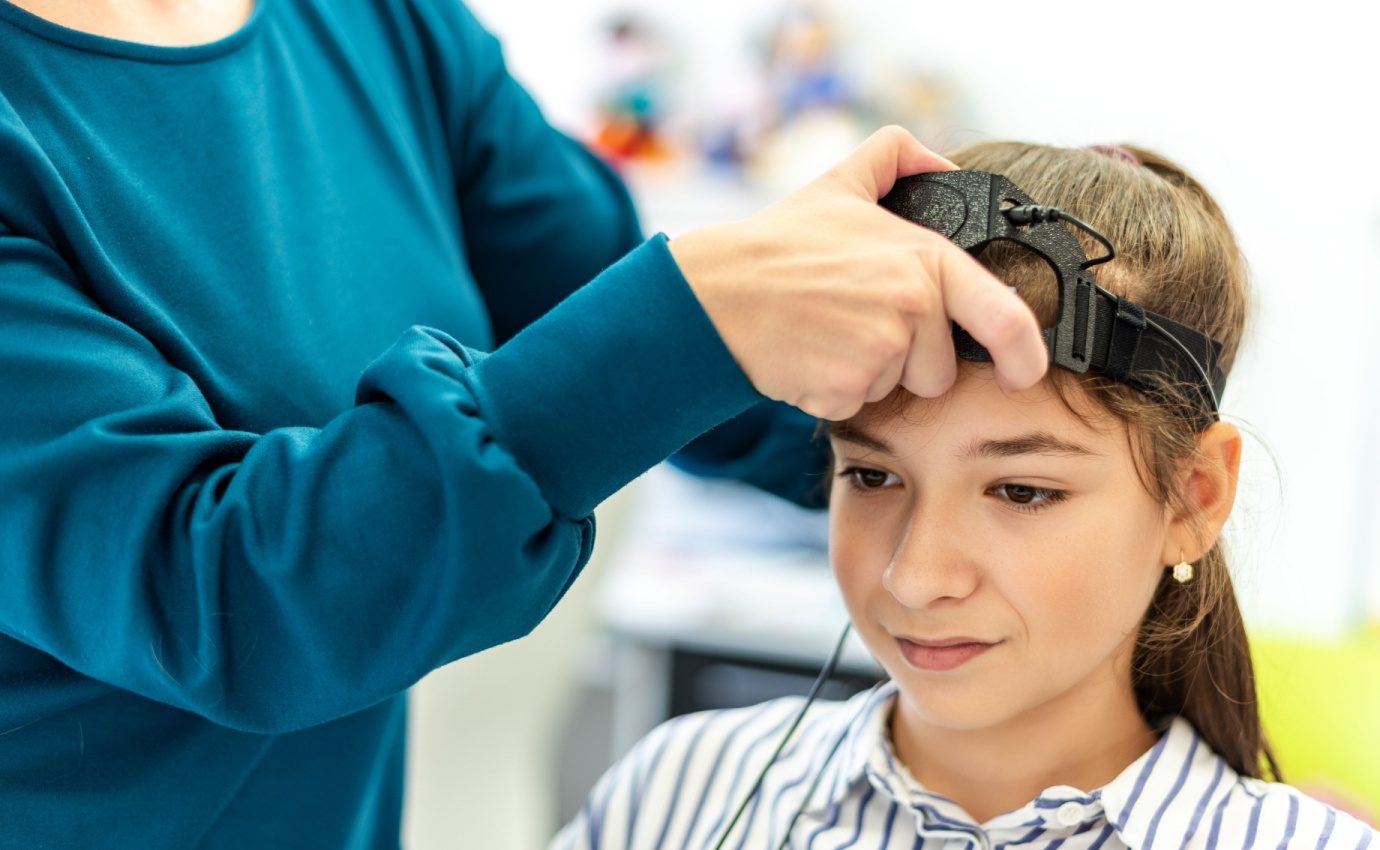 Ein junges Mädchen nimmt an einer EEG-Neurofeedback-Sitzung teil, während eine Therapeutin die Geräte justiert. Biofeedback ist eine wirksame Methode zur Reduzierung von Angst bei Kindern, indem es ihnen hilft, ihre körperlichen Reaktionen zu kontrollieren.