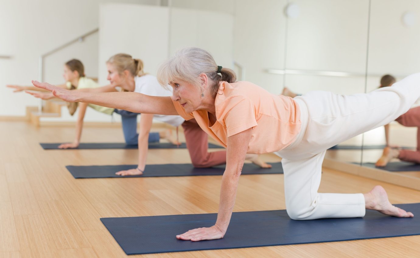 Ältere Frau führt Yoga-Übung im Kursraum aus, um chronische Rückenschmerzen zu lindern. Studie zeigt, dass Yoga effektiv bei der Reduktion von Rückenschmerzen sein kann.