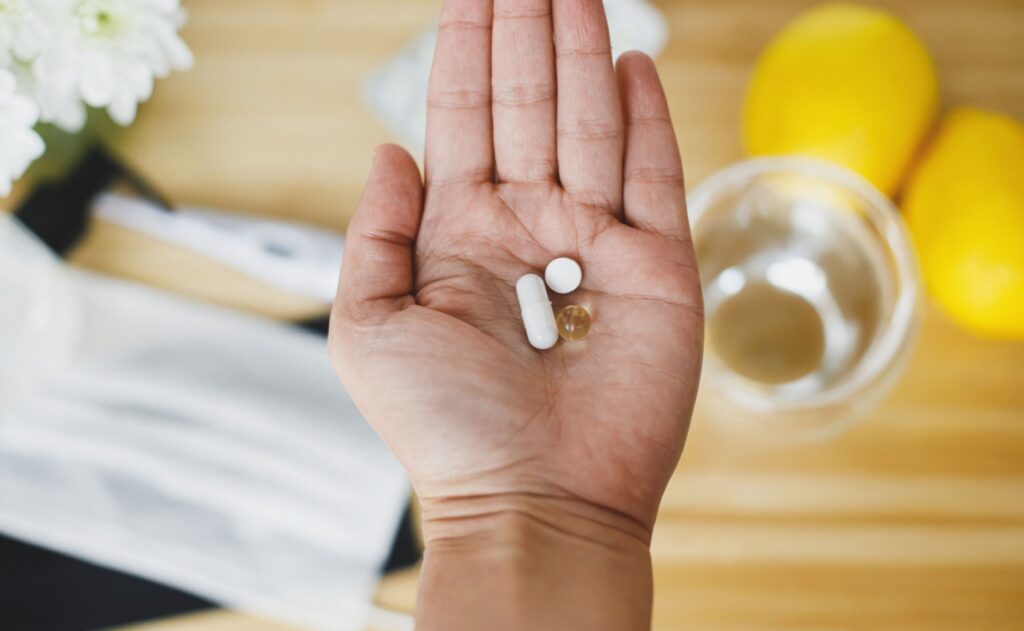 Hand hält Zink-, Vitamin D- und Vitamin C-Tabletten zur Bekämpfung von Erkältungen. Eine neue Cochrane-Review untersucht die Wirksamkeit von Zink bei der Vorbeugung und Behandlung von Erkältungen.