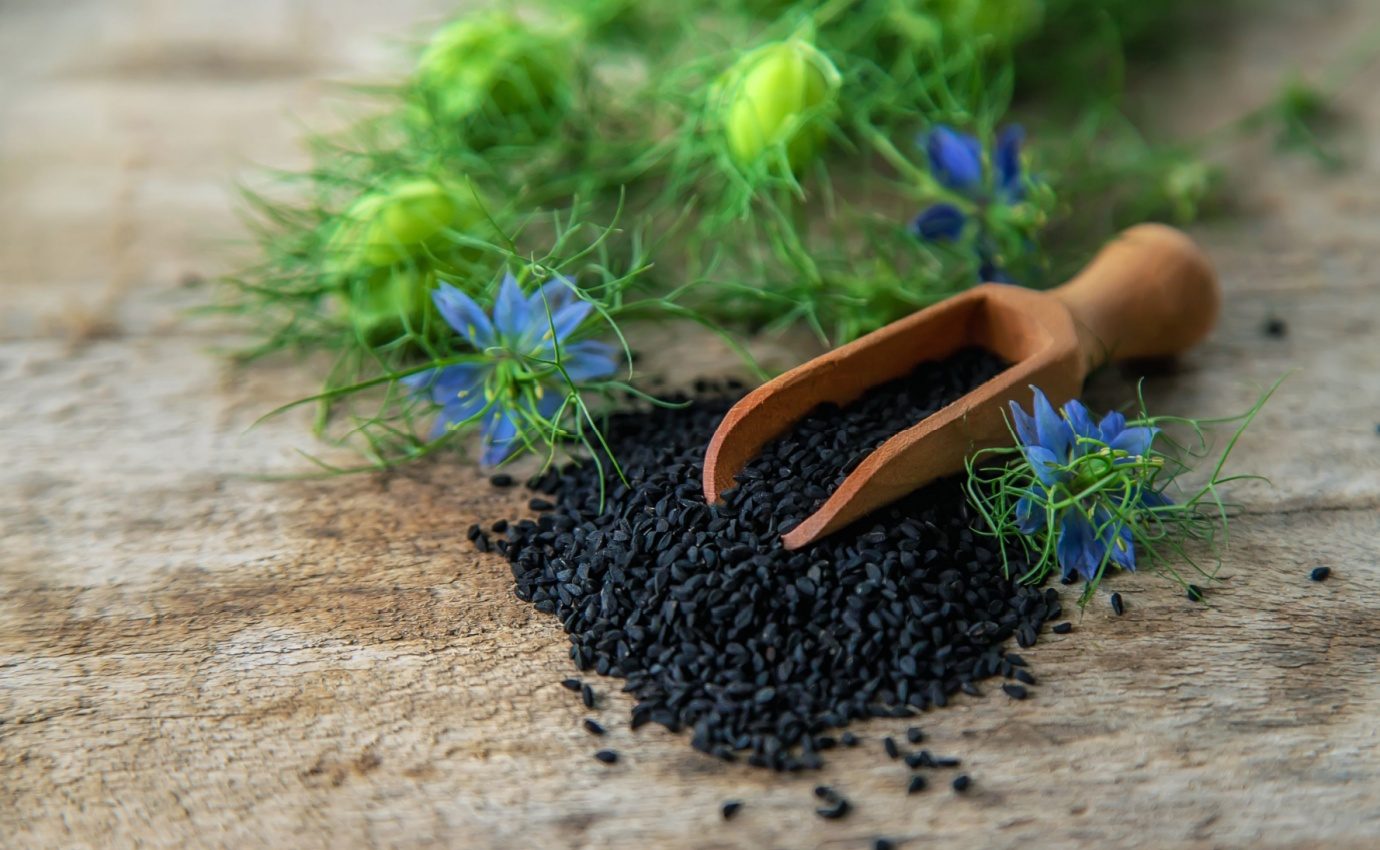 Schwarzkümmelsamen und blaue Blüten auf rustikalem Holzhintergrund, illustrierend die Nutzung mediterraner Heilkräuter in der natürlichen Blutzuckerkontrolle bei Typ-2-Diabetes.