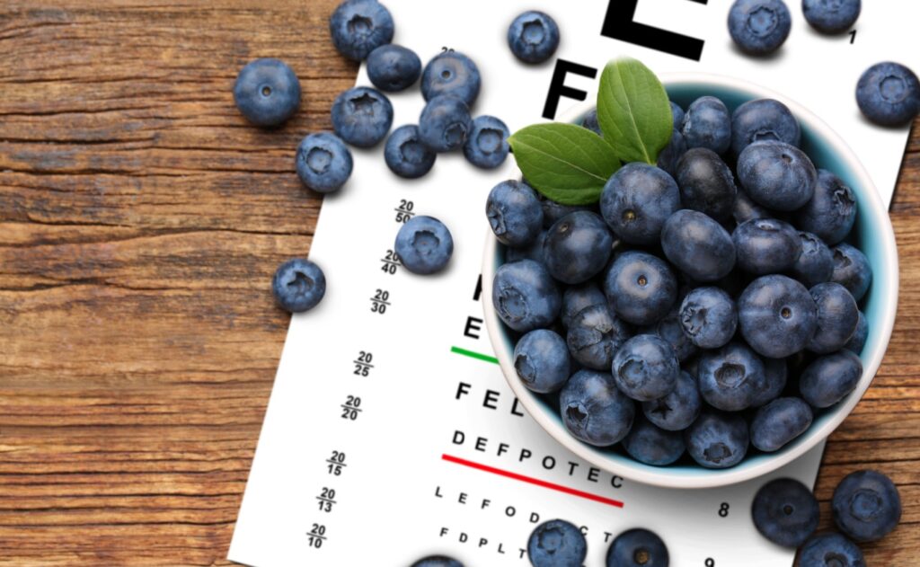 Schale mit frischen Heidelbeeren auf einem Sehtest-Diagramm, symbolisierend die mögliche Rolle von Antioxidantien bei der Verzögerung des Fortschreitens der altersbedingten Makuladegeneration (AMD).