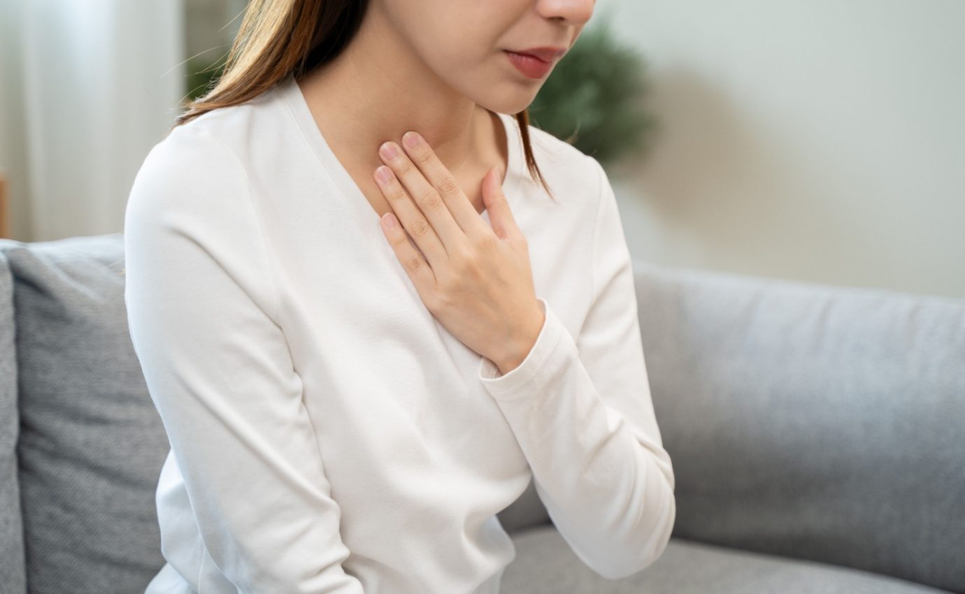 Eine Frau legt ihre Hand auf den Halsbereich, möglicherweise aufgrund von Sodbrennen oder Refluxbeschwerden. Der Artikel vergleicht die Wirkung der natürlichen Alternative Poliprotect mit dem herkömmlichen Säureblocker Omeprazol bei der Behandlung von Sodbrennen.