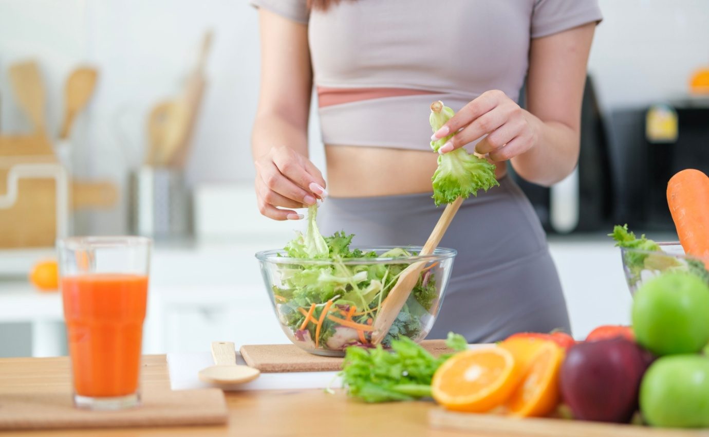 Gesunde Ernährung als Schlüssel zum Abnehmerfolg: Eine Frau bereitet in einer modernen Küche einen frischen Salat mit Gemüse und Obst zu. Stiftung Warentest hat 15 Diätkonzepte untersucht – nur wenige konnten überzeugen.