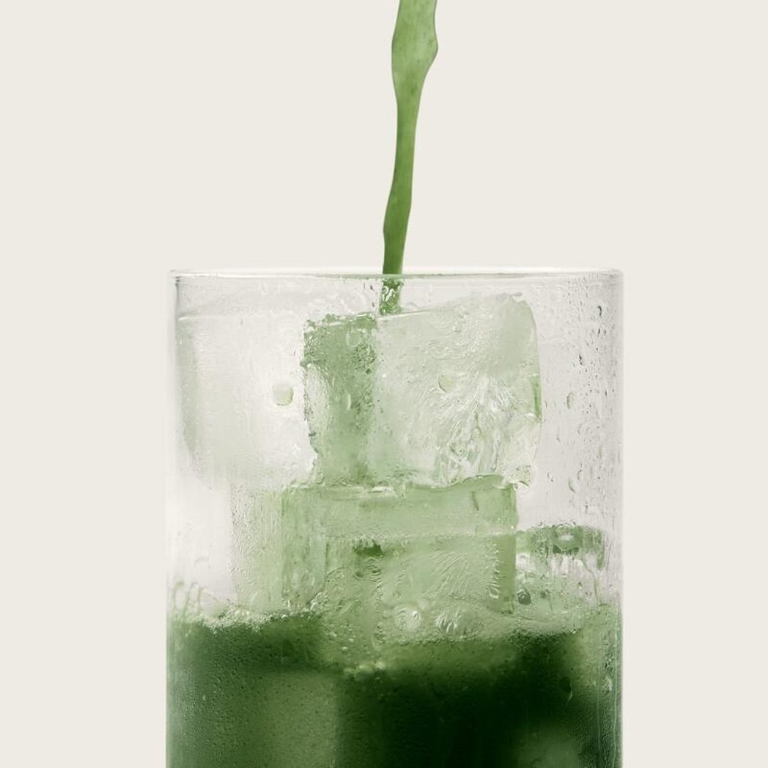 Grüner AG1-Drink wird mit Eiswürfeln in ein Glas gegossen – erfrischender Nährstoffkick