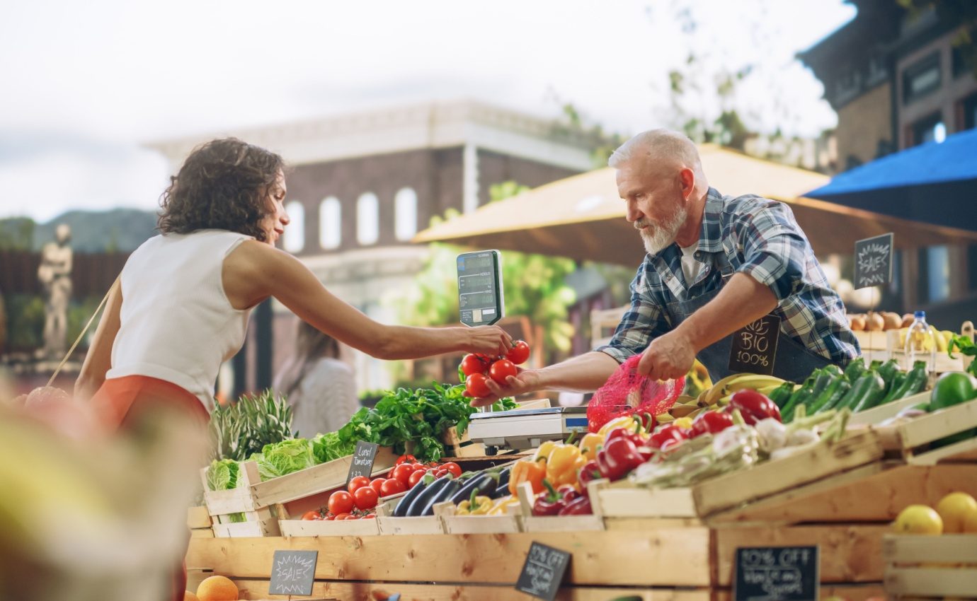 Frau kauft frisches Gemüse auf einem mediterranen Wochenmarkt – Symbol für regionale, nachhaltige Ernährung im Stil der Mittelmeerdiät.